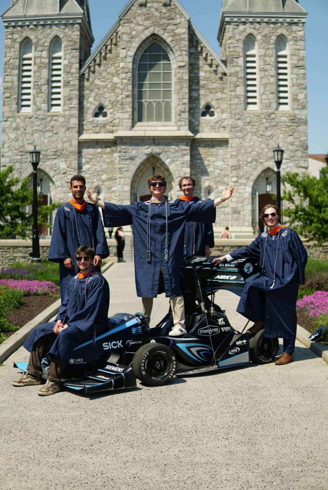 Some of the VU17 seniors in graduation gowns with the car outside a campus church